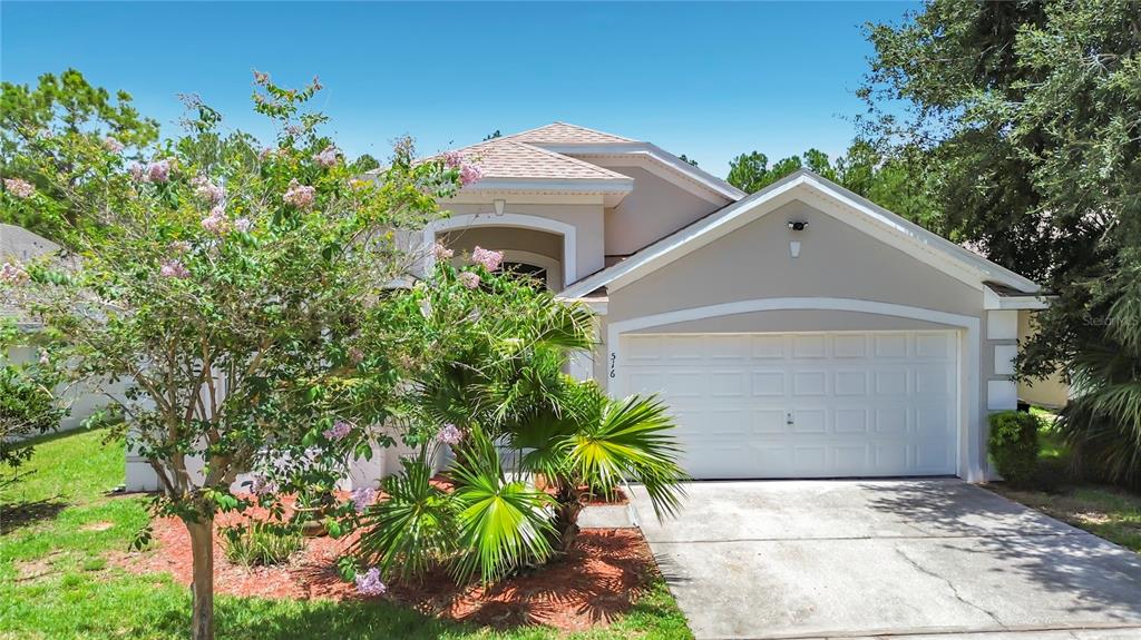 A beige single-story house with a white garage door and a palm tree in front — 516 PINE CONE DRIVE, DAVENPORT, FL
