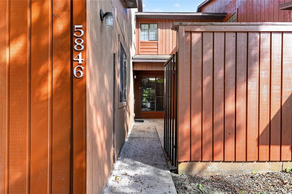 A concrete walkway leads to a recessed front entrance between two vertical wood-paneled walls — 5846 SW 9TH PLACE, GAINESVILLE, FL