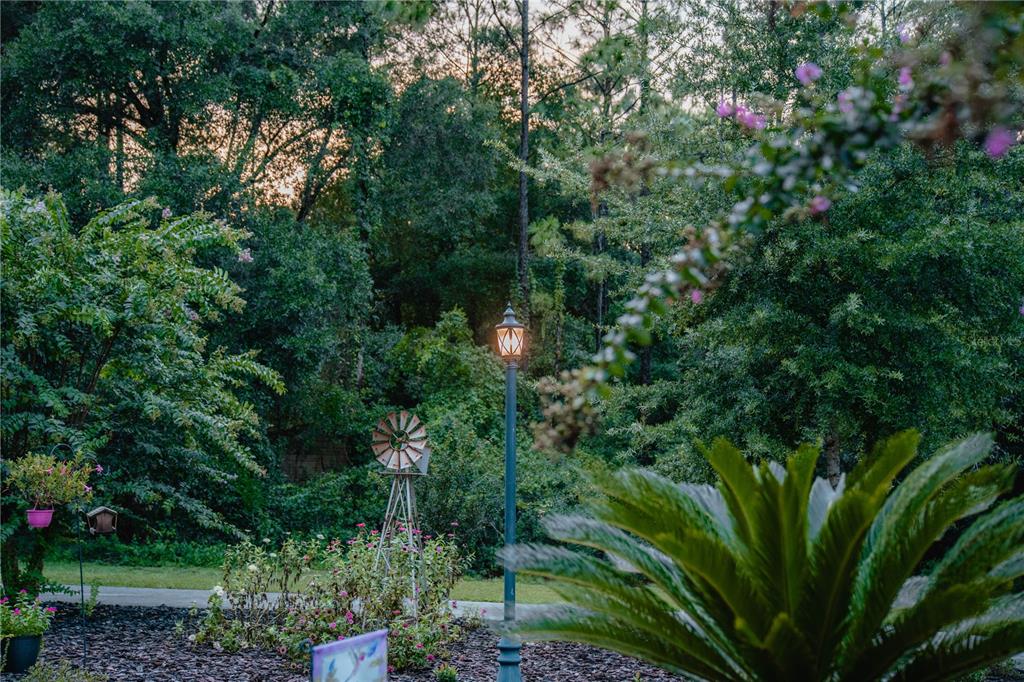 A backyard garden features a decorative windmill, a tall lamp post, and lush green trees — 12009 S DAFFODIL POINT, FLORAL CITY, FL
