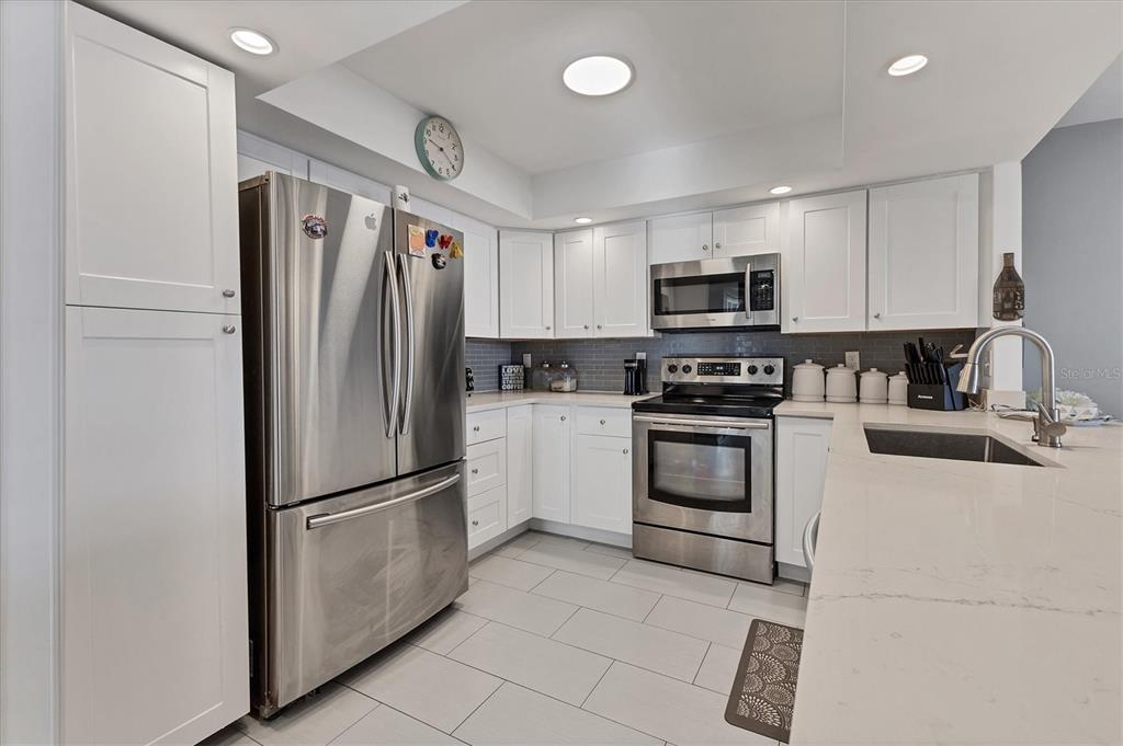 A kitchen features white cabinets, stainless steel appliances, gray tile flooring, and quartz countertops — 101 S GULFSTREAM AVENUE UNIT 15E, SARASOTA, FL