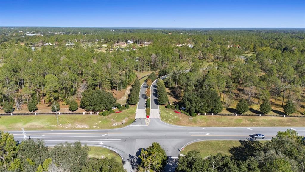 An aerial view shows a gated community entrance intersecting with a paved road — 24250 DEEP SPRINGS LOOP, EUSTIS, FL