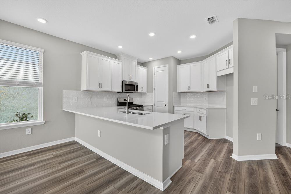 A modern kitchen features white cabinetry, quartz countertops, and a staircase with dark railings — 13419 COMMONS AVENUE, PARRISH, FL