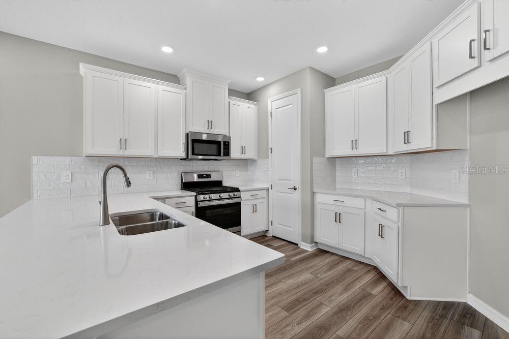 A modern kitchen features white cabinets, a quartz island, and wood-look flooring — 13419 COMMONS AVENUE, PARRISH, FL