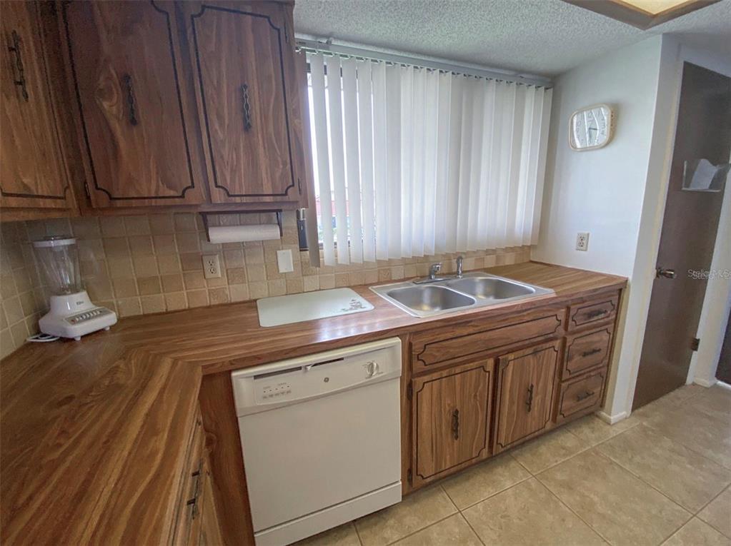 A kitchen features wood cabinets, laminate countertops, a white dishwasher, and a double-basin sink — 9940 EAGLES POINT CIRCLE UNIT 4, PORT RICHEY, FL