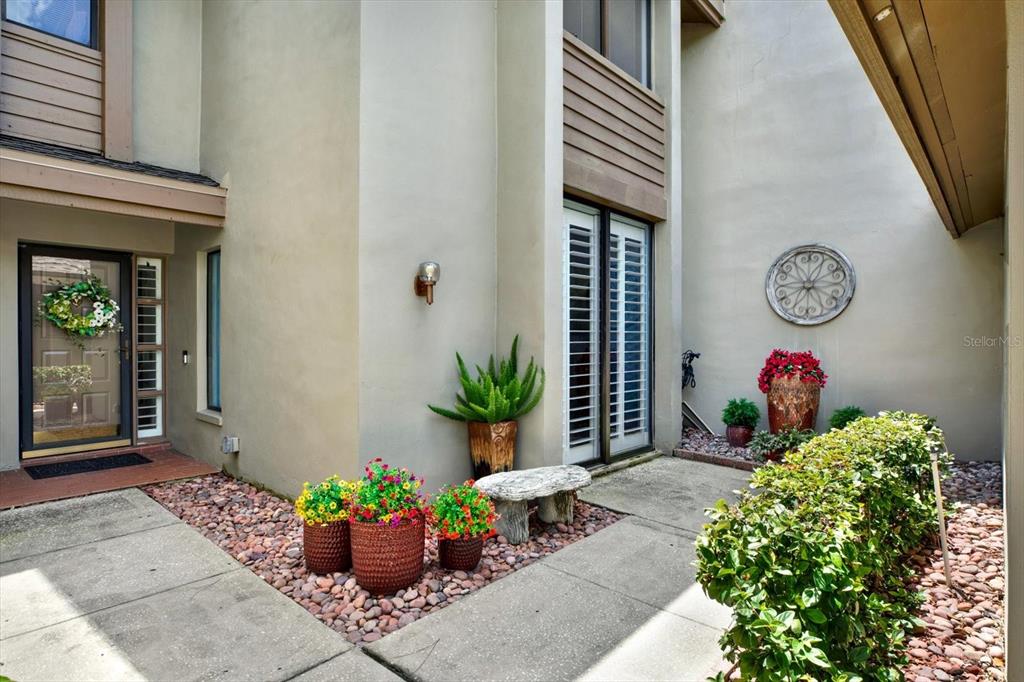 A concrete walkway leads to a front entrance with potted flowers and a stone bench — 3090 LANDMARK BOULEVARD UNIT 1904, PALM HARBOR, FL