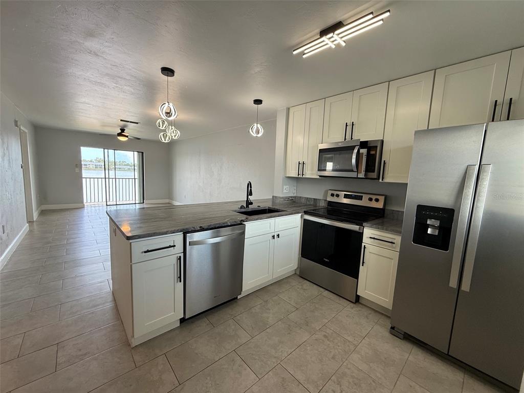 A kitchen with white cabinets, stainless steel appliances, and a dark countertop overlooks a living area — 25225 RAMPART BOULEVARD UNIT 2005, PUNTA GORDA, FL
