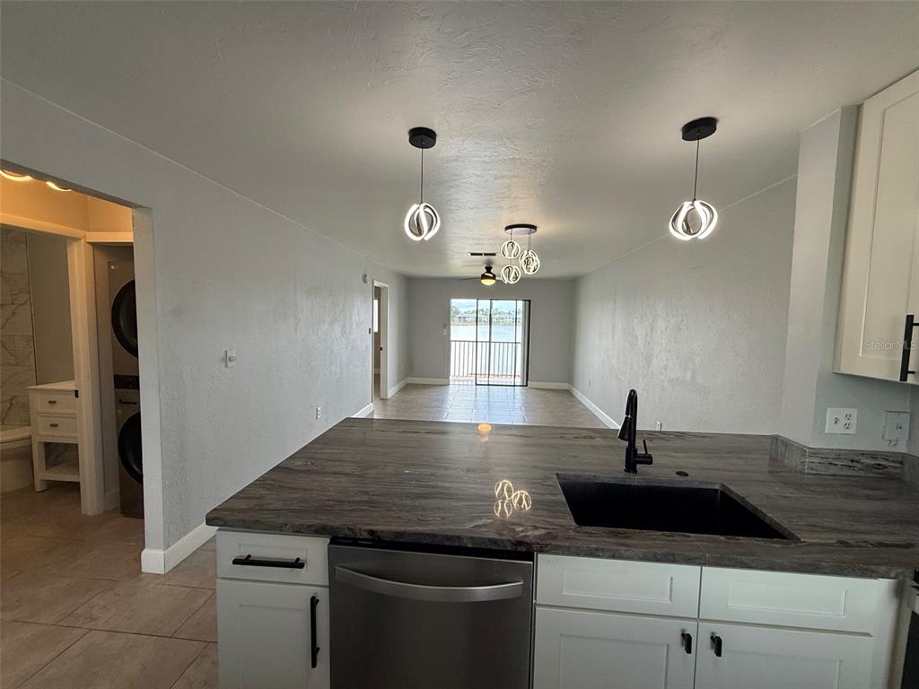 A kitchen with dark stone countertops and white cabinets overlooks a living area with water views — 25225 RAMPART BOULEVARD UNIT 2005, PUNTA GORDA, FL