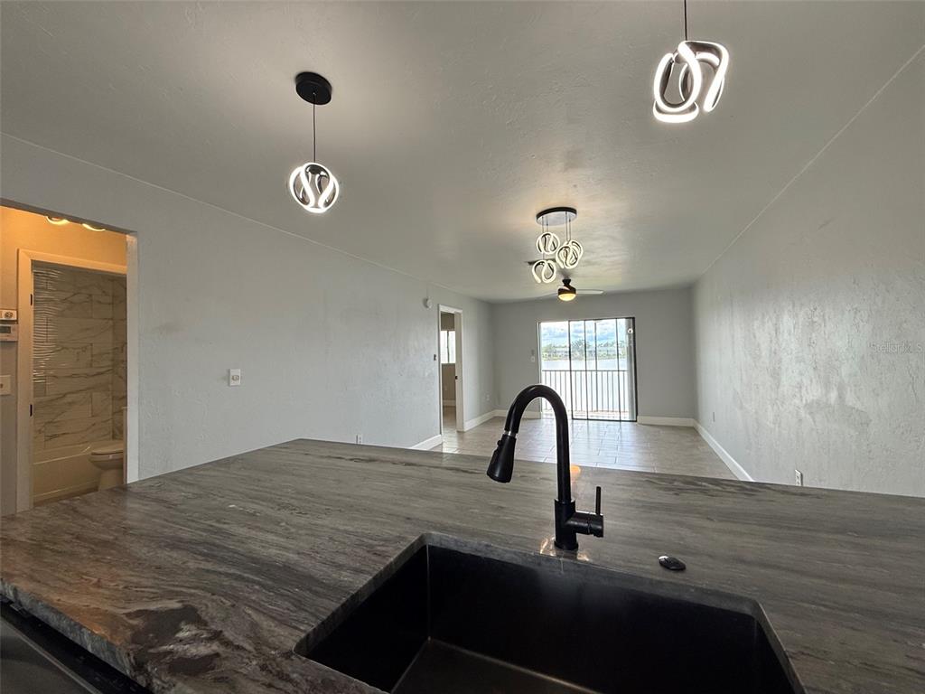 A kitchen island with a dark stone countertop and black sink overlooks a living area — 25225 RAMPART BOULEVARD UNIT 2005, PUNTA GORDA, FL