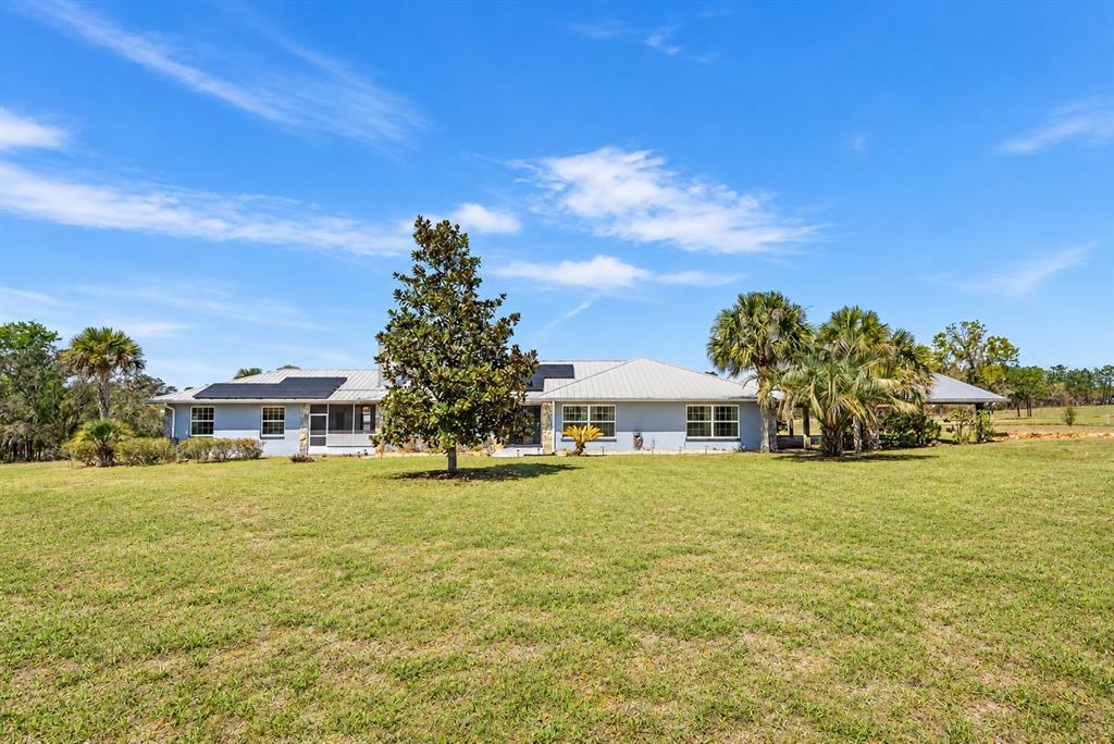 A single-story house with a metal roof, solar panels, and stone accents sits on grass — 7450 SE STATE ROAD 121, MORRISTON, FL