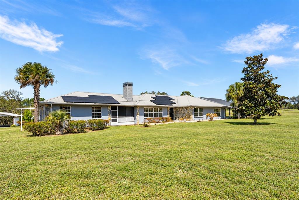 An aerial view shows a blue, single-story house with solar panels on a metal roof — 7450 SE STATE ROAD 121, MORRISTON, FL