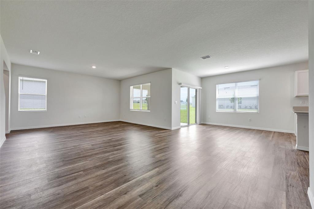An open-concept living area features light gray walls, wood-look flooring, and several windows — 3610 PFEIFFER FALLS PLACE, DAVENPORT, FL