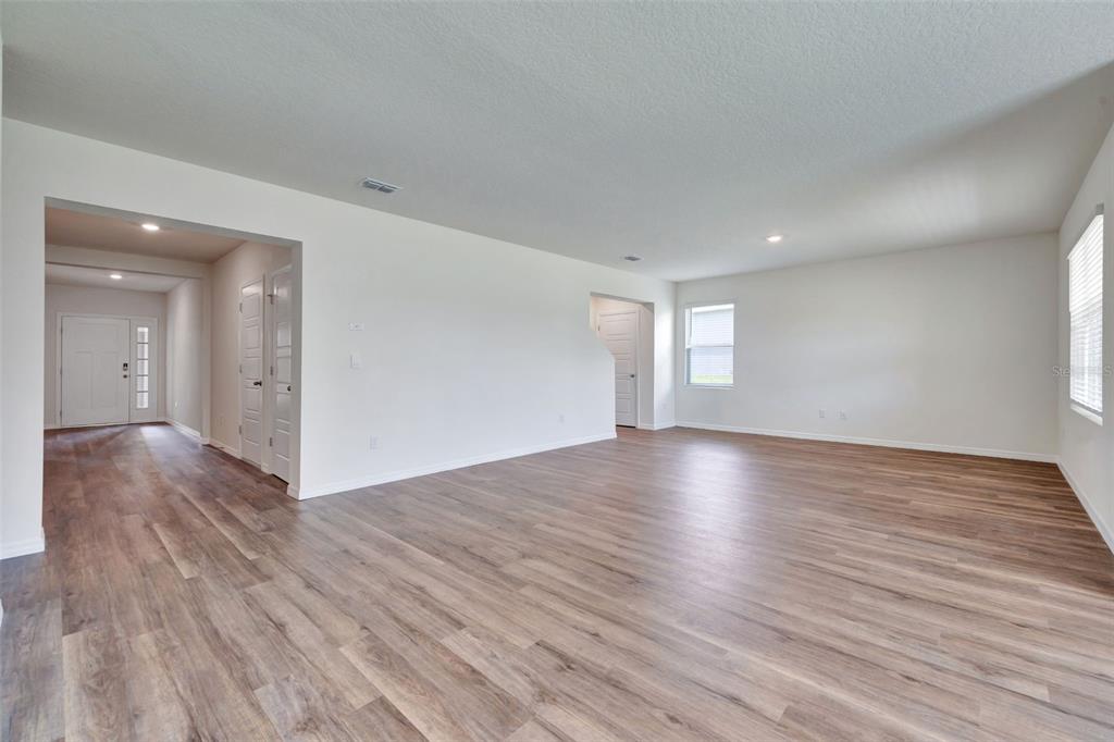 An open-concept living area features light-colored walls, wood-look flooring, and a view of the entryway — 3610 PFEIFFER FALLS PLACE, DAVENPORT, FL