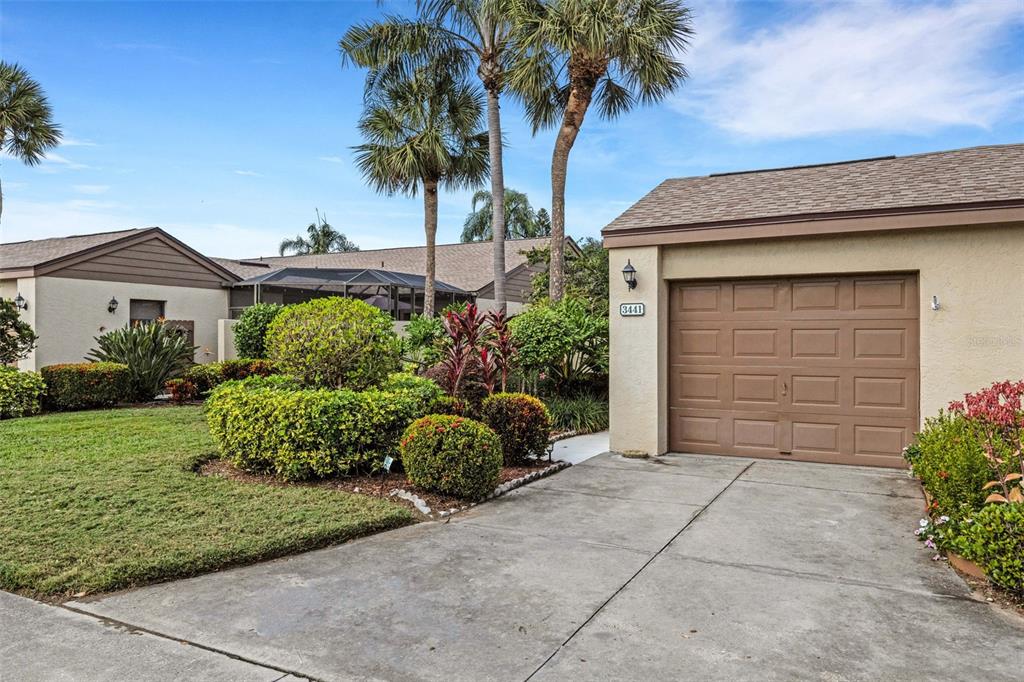 A single-story house exterior features a brown garage door, concrete driveway, and landscaped front yard — 3441 BEEKMAN PLACE UNIT 40, SARASOTA, FL