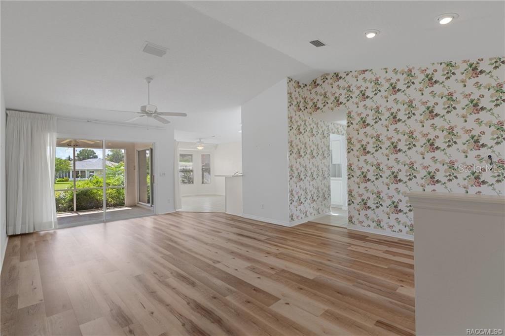 A living room with light wood flooring, a floral wallpaper accent wall, and sliding glass doors — 4589 N GRASS ISLAND TERRACE, HERNANDO, FL