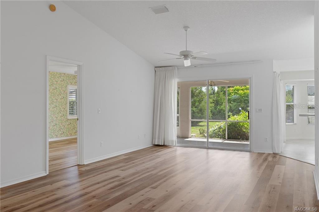A bright living room features wood-look flooring, a vaulted ceiling, and sliding glass patio doors — 4589 N GRASS ISLAND TERRACE, HERNANDO, FL