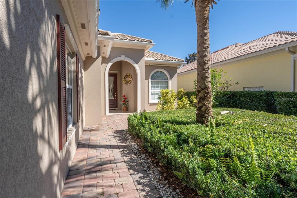 A paved walkway leads to the arched entryway of a stucco home with a palm tree — 11731 EAGLE RAY LANE, ORLANDO, FL