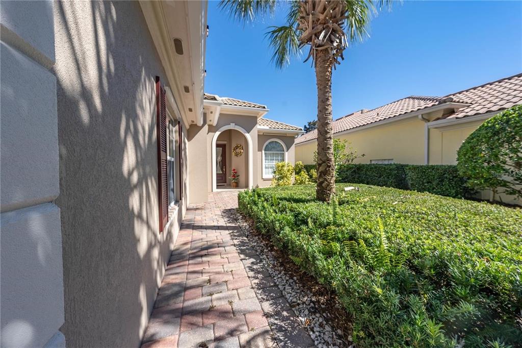 A paved walkway leads to the arched entryway of a tan house with a palm tree — 11731 EAGLE RAY LANE, ORLANDO, FL