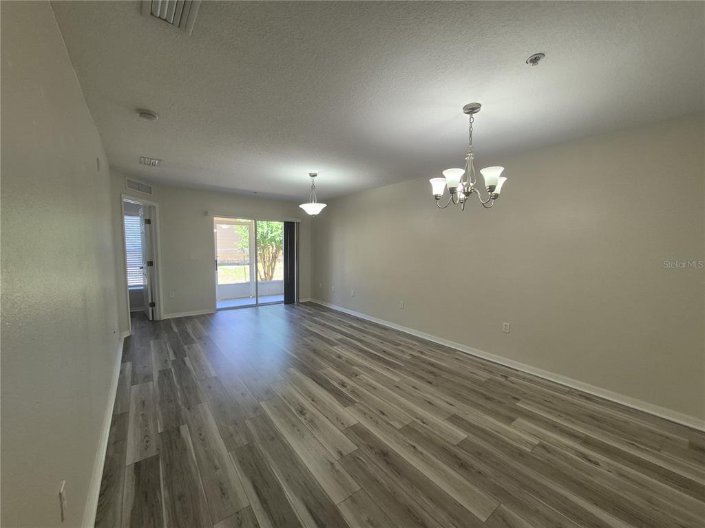 A bedroom features light wood-look flooring, a bed with a grey comforter, and a corner desk — 2720 CLUB CORTILE CIRCLE UNIT A, KISSIMMEE, FL