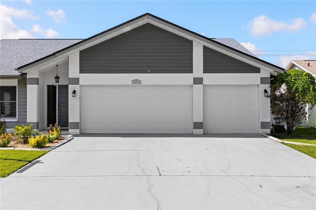The exterior of a house features a two-car garage, a concrete driveway, and white brick accents — 12212 STEPPINGSTONE BOULEVARD, TAMPA, FL