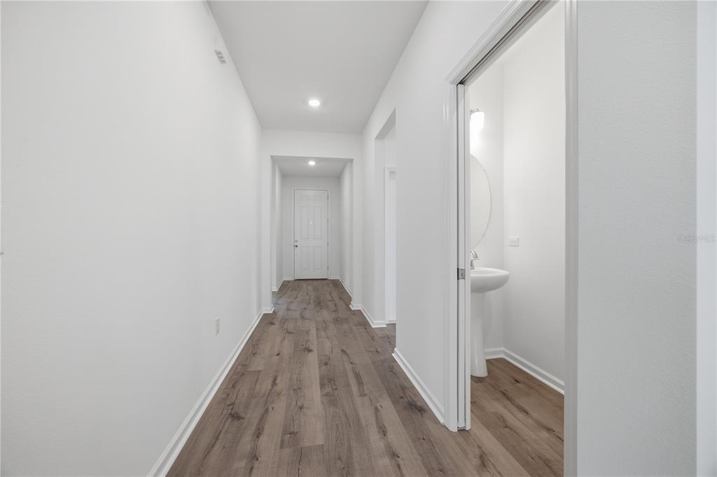 A hallway with wood-look flooring leads to a closed door and a small powder room — 5715 HIAWASSEE ROAD, LEESBURG, FL