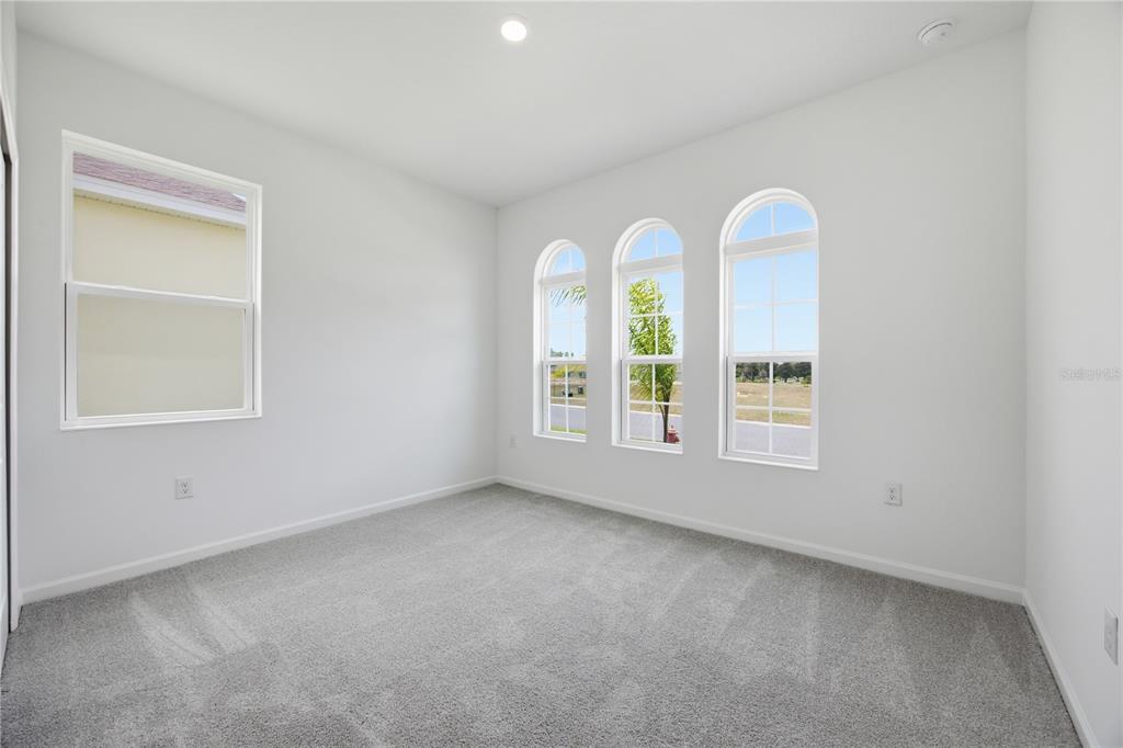 An empty bedroom with gray carpet, white walls, and three arched windows overlooking a field — 5715 HIAWASSEE ROAD, LEESBURG, FL