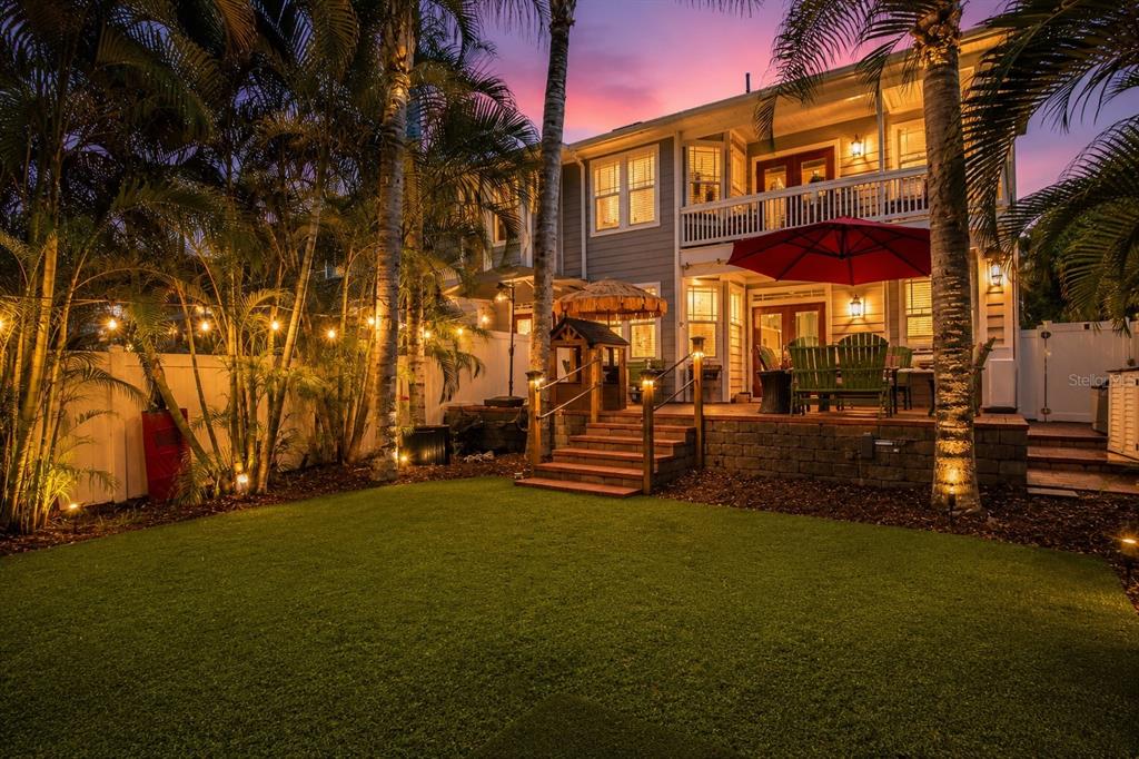 A brick patio features a dining set under a red umbrella with string lights above — 2869 BAYSHORE TRAILS DRIVE, TAMPA, FL