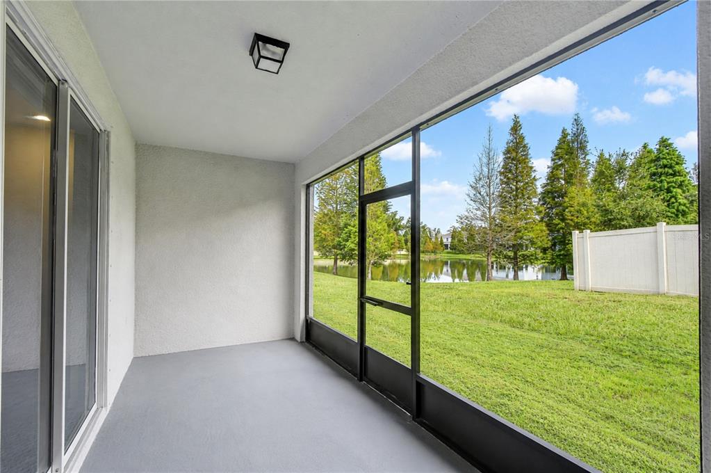 A screened-in porch with gray flooring overlooks a grassy backyard, a pond, and tall trees — 3326 PLEASANT WILLOW COURT, BRANDON, FL