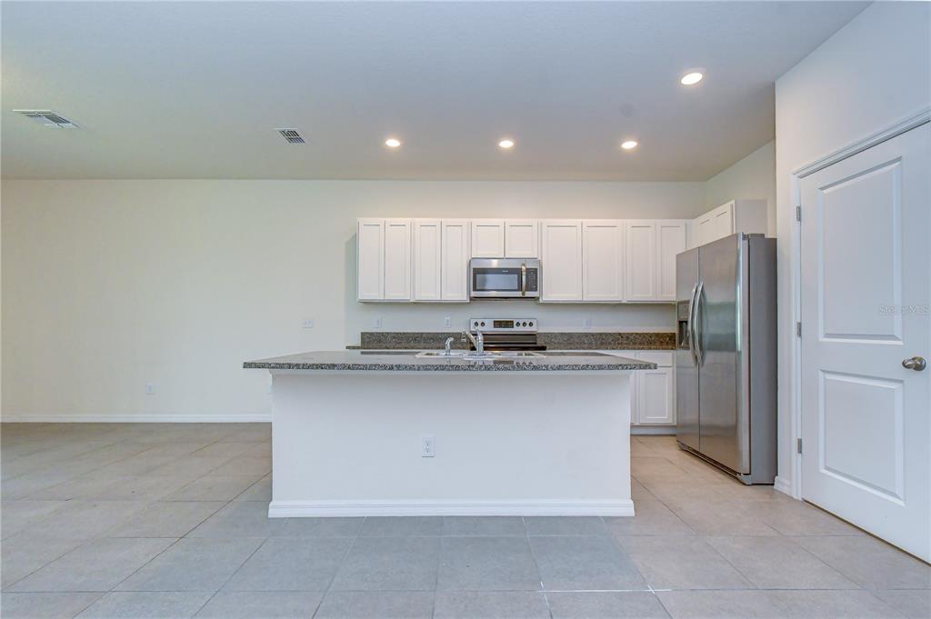 A kitchen features white cabinets, stainless steel appliances, a granite island, and light tile flooring — 3326 PLEASANT WILLOW COURT, BRANDON, FL