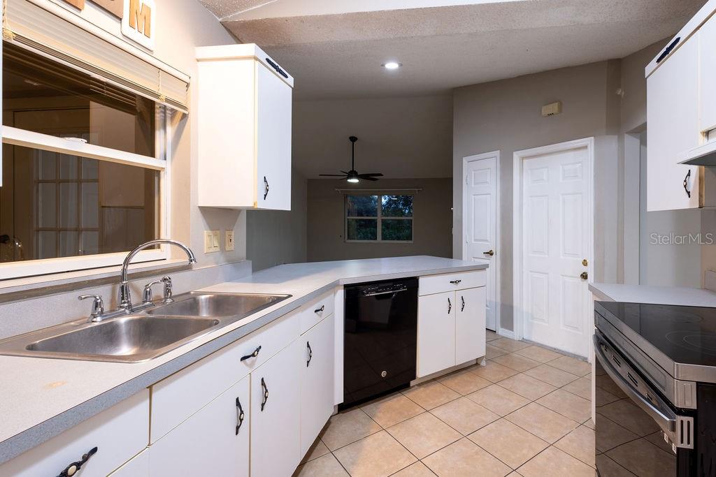 A kitchen with white cabinets, a black dishwasher, and a double sink overlooks a living area — 1570 S BISCAYNE DRIVE, NORTH PORT, FL