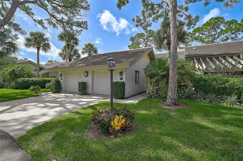 A single-story house with a two-car garage, a paved driveway, and surrounding palm trees — 3217 SANDLEHEATH UNIT 45, SARASOTA, FL