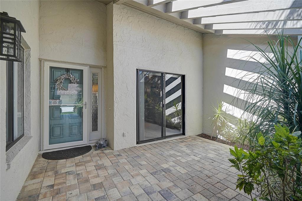 A paved entryway features a blue front door, a sliding glass door, and a pergola — 3217 SANDLEHEATH UNIT 45, SARASOTA, FL