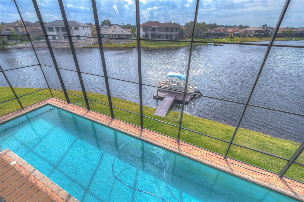 A screened-in pool overlooks a lake with a private dock and a pontoon boat — 10602 CAYMAN ISLE COURT, TAMPA, FL