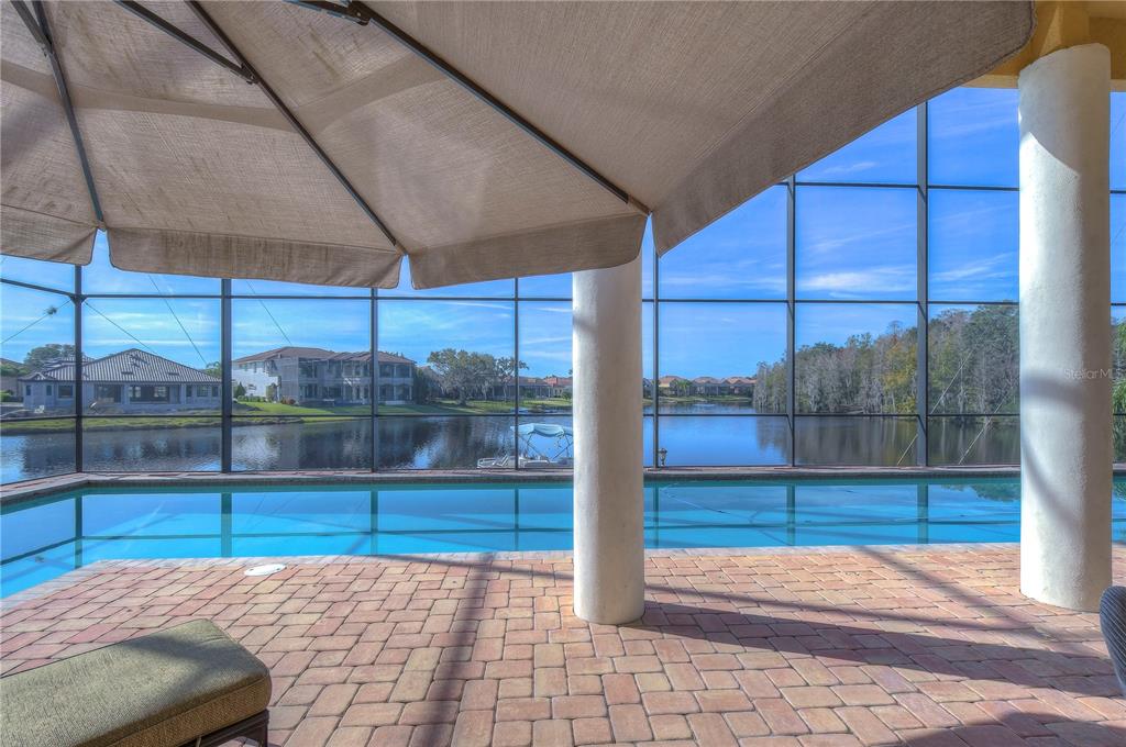 A screened-in pool patio overlooks a lake with houses in the background — 10602 CAYMAN ISLE COURT, TAMPA, FL
