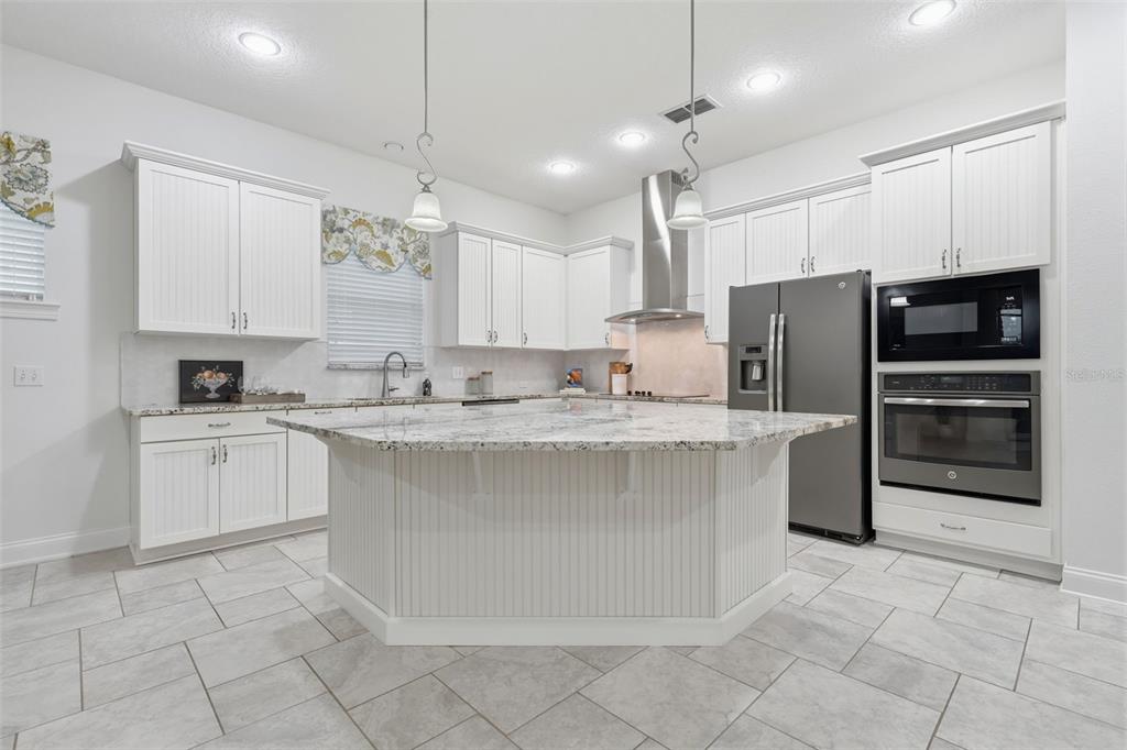 A kitchen with white beadboard cabinetry, a large granite island, and stainless steel appliances — 16716 ABBEY HILL COURT, CLERMONT, FL