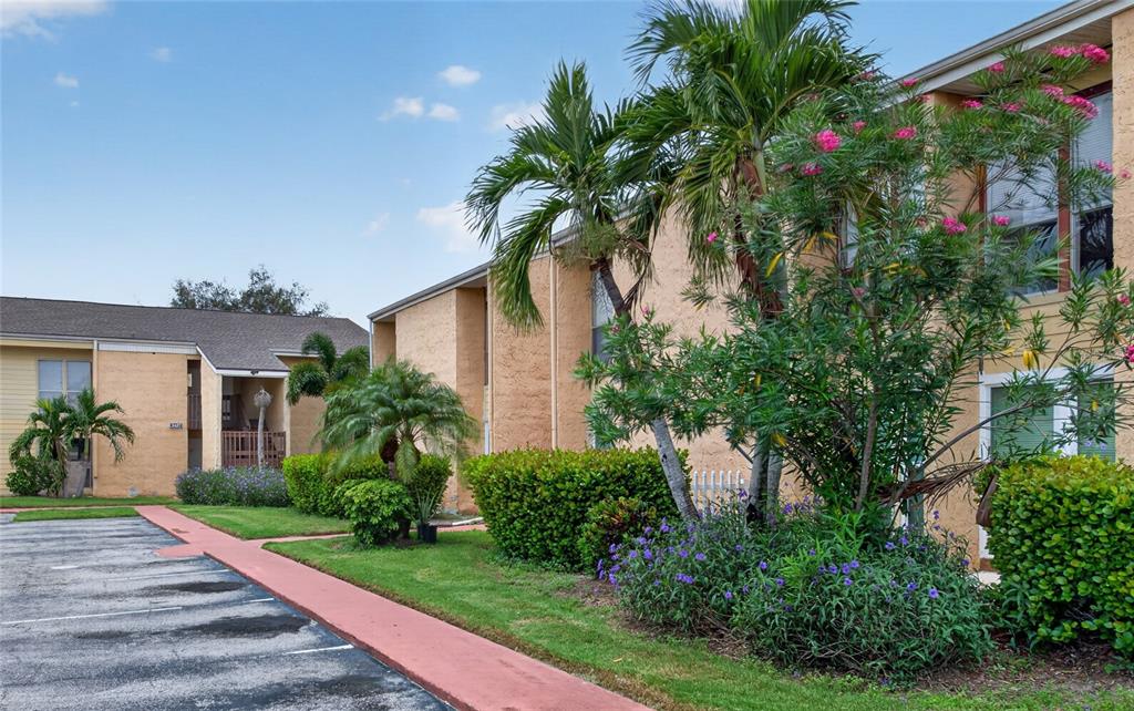 Exterior view of a multi-story apartment building with palm trees, landscaping, and a parking lot — 3461 CLARK ROAD UNIT 160, SARASOTA, FL