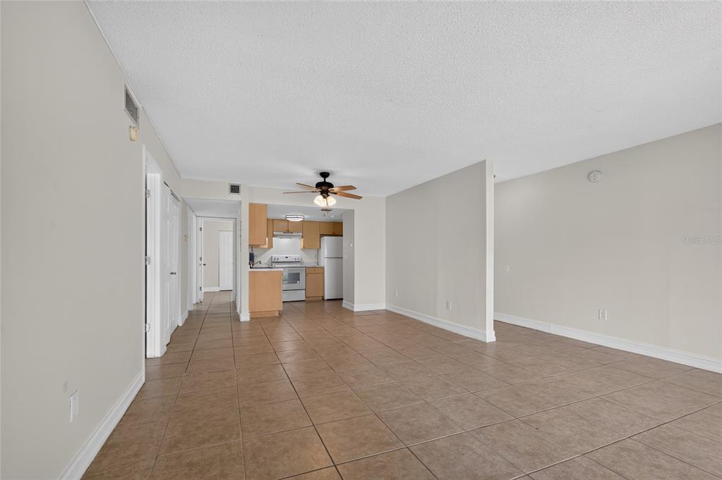 An open-concept living area with tan tile flooring leads to a kitchen with light wood cabinets — 3461 CLARK ROAD UNIT 160, SARASOTA, FL