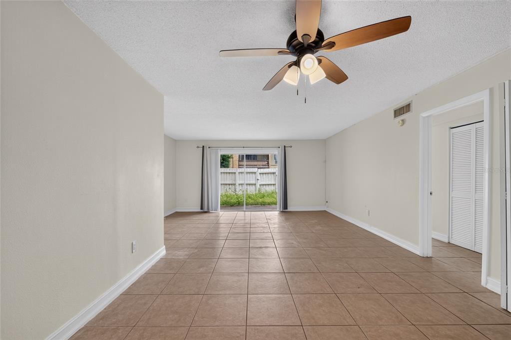 An empty living room with tan tile flooring, a ceiling fan, and sliding glass doors — 3461 CLARK ROAD UNIT 160, SARASOTA, FL