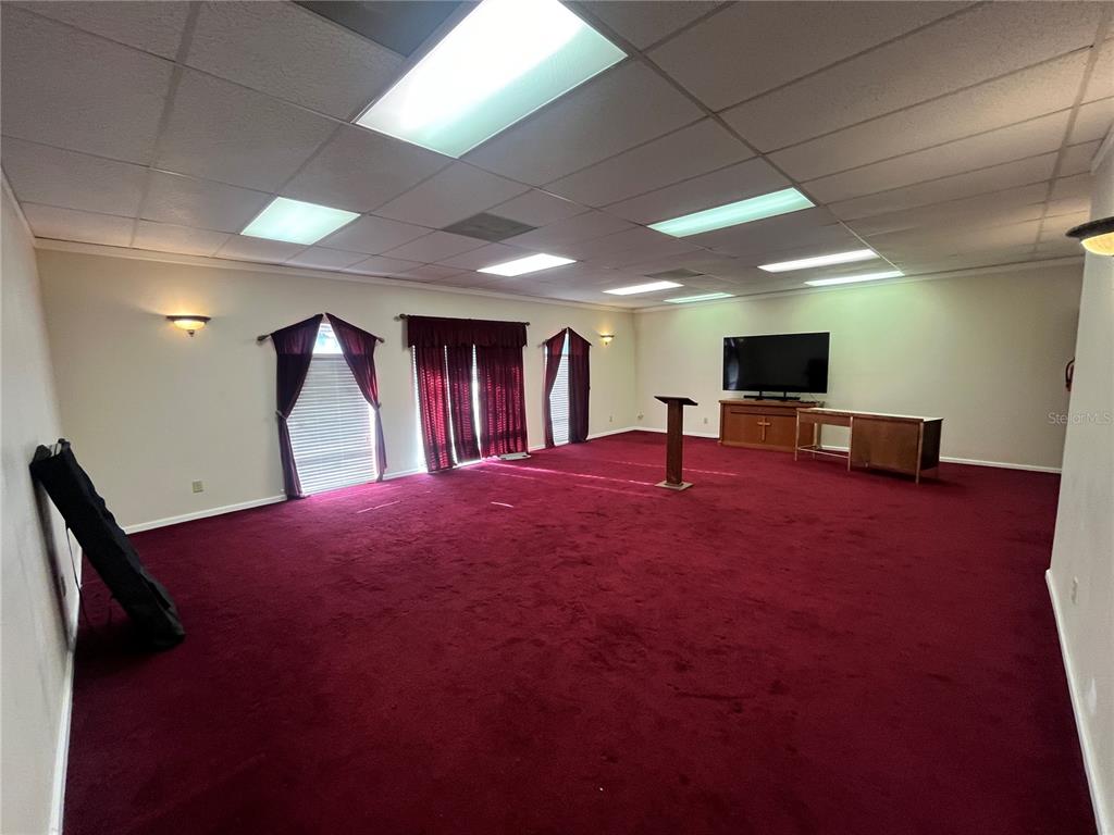 A large room with red carpeting, a drop ceiling, and a television on a stand — 1165 1ST STREET S UNIT 1165, WINTER HAVEN, FL