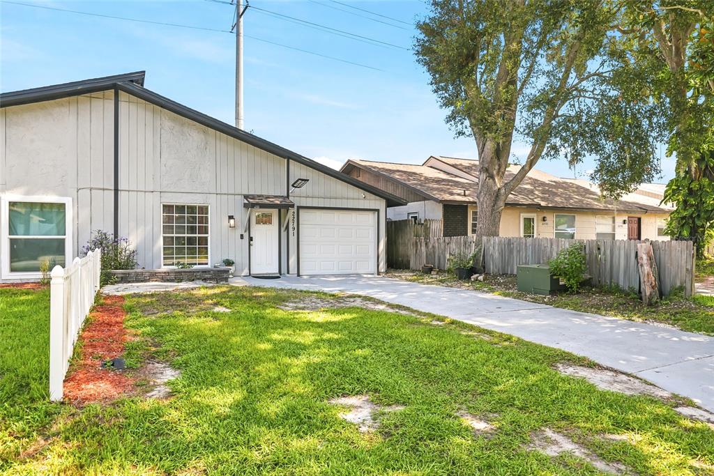 A single-story house with light gray vertical siding, a white garage door, and a front lawn — 22791 PENNY LOOP, LAND O LAKES, FL