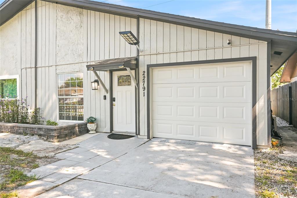 The exterior of a house features a white garage door, a front entrance, and vertical siding — 22791 PENNY LOOP, LAND O LAKES, FL