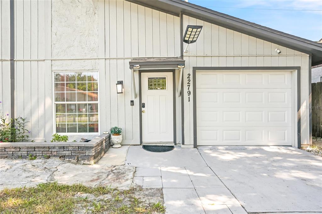 The exterior of a house features vertical siding, a white front door, and a garage — 22791 PENNY LOOP, LAND O LAKES, FL