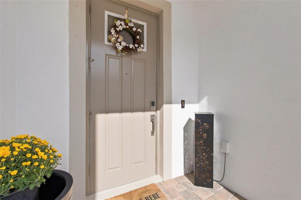 A tan front door with a floral wreath stands on a paved porch — 18623 NOBLE CASPIAN DRIVE, LUTZ, FL