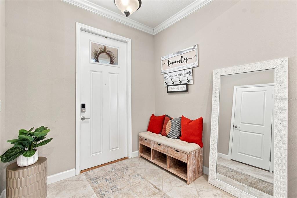 An entryway features a white front door, a wooden bench with red pillows, and a mirror — 18623 NOBLE CASPIAN DRIVE, LUTZ, FL