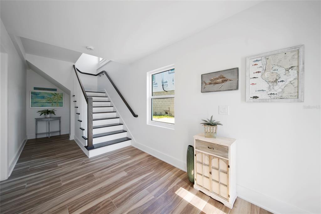 An entryway features wood-look tile flooring, a staircase with dark railings, and coastal wall decor — 15564 BERTRAM DRIVE, HUDSON, FL