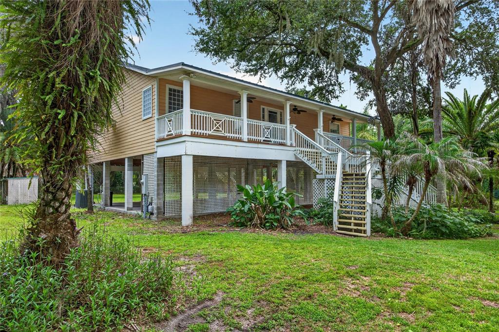 A two-story house with tan siding, a raised porch, and lattice skirting stands on grass — 8435 FLORENCE COVE ROAD, ST AUGUSTINE, FL