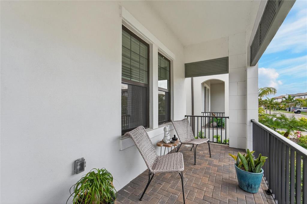 A covered balcony features brick flooring, two wicker chairs, and a metal railing — 1071 SEAGRAPE DRIVE, RUSKIN, FL