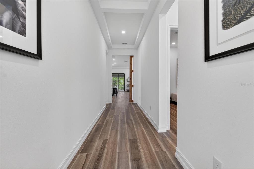 A hallway with wood-look flooring leads toward a bright living area with a sliding door — 1071 SEAGRAPE DRIVE, RUSKIN, FL