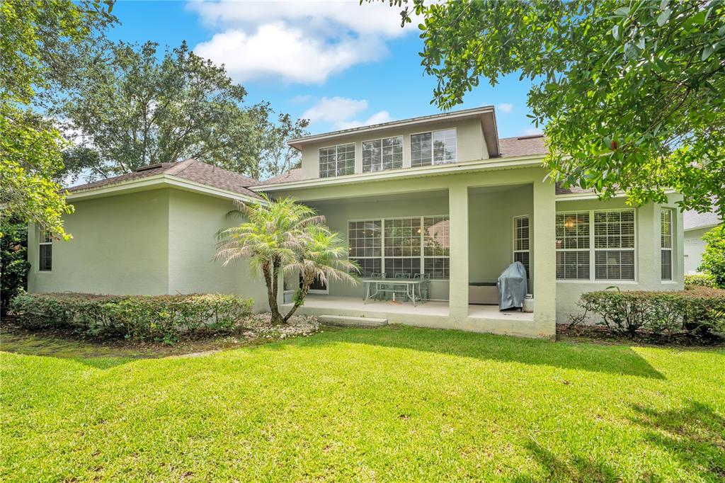 The exterior of a light green house features a covered patio, lawn, and mature trees — 8344 BOWDEN WAY, WINDERMERE, FL