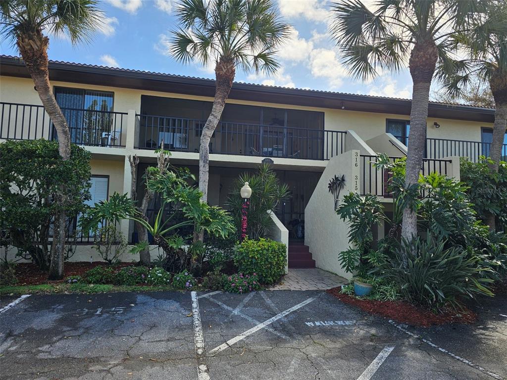 A two-story apartment building features balconies, palm trees, and a paved parking lot in front — 6468 SEAGULL DRIVE UNIT 316, BRADENTON, FL