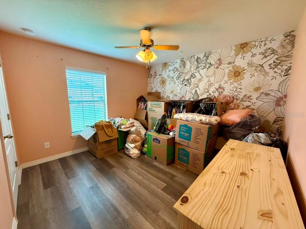 A bedroom with wood-look flooring, a floral accent wall, and several cardboard moving boxes — 1609 STEELY DRIVE, DUNDEE, FL